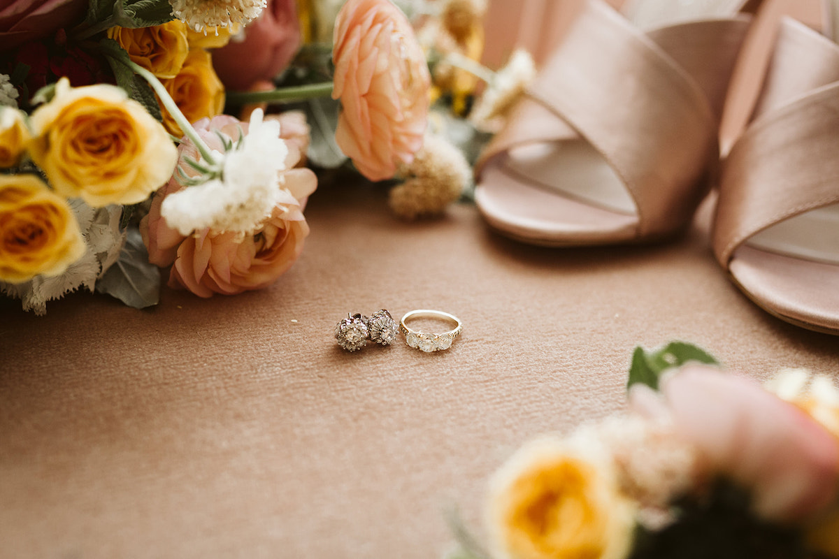 Bride's diamond earrings, wedding band, champagne colored heels surrounded by bouquets.