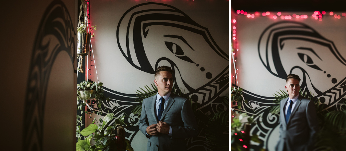 Groom stands in front of window and tall indoor plants. Red sparkle lights line a white wall with contrasting black artwork