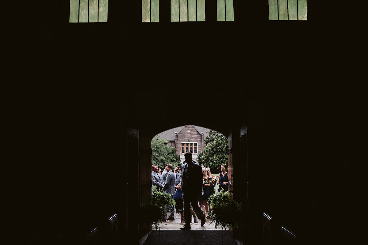 Wedding party gathers outside the front doors of Patten Chapel. Deep shadowy interior contrasts with bright sky outside.