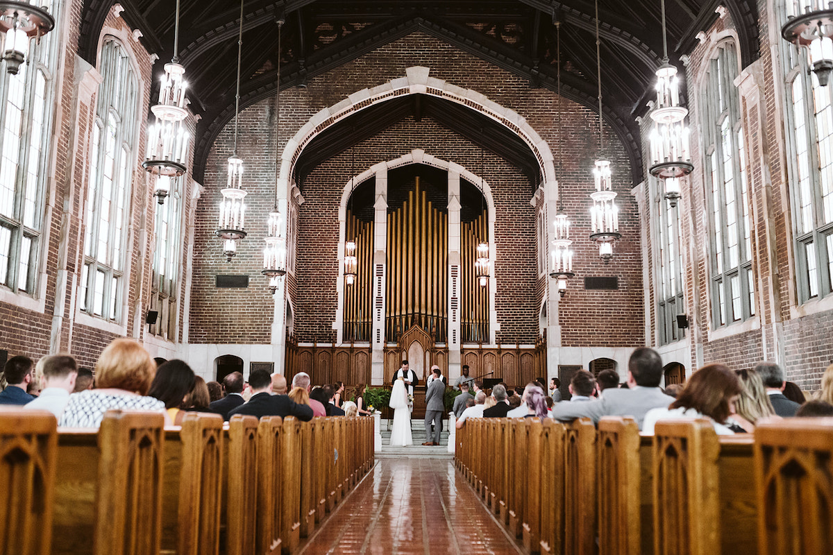 Brick arched sanctuary of Patten Chapel with large pipe organ at the front. Guests sit in wooden pews at wedding ceremony.