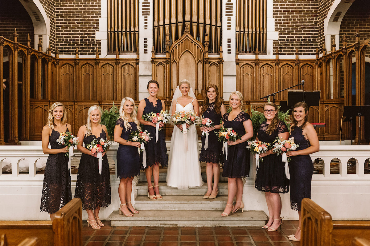 Bride and bridesmaids stand on stone steps of church altar in front of large organ pipes