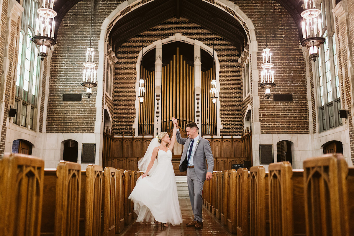 Groom twirls bride between wooden pews in front of large organ pipes in the arched brick sanctuary of Patten Chapel.