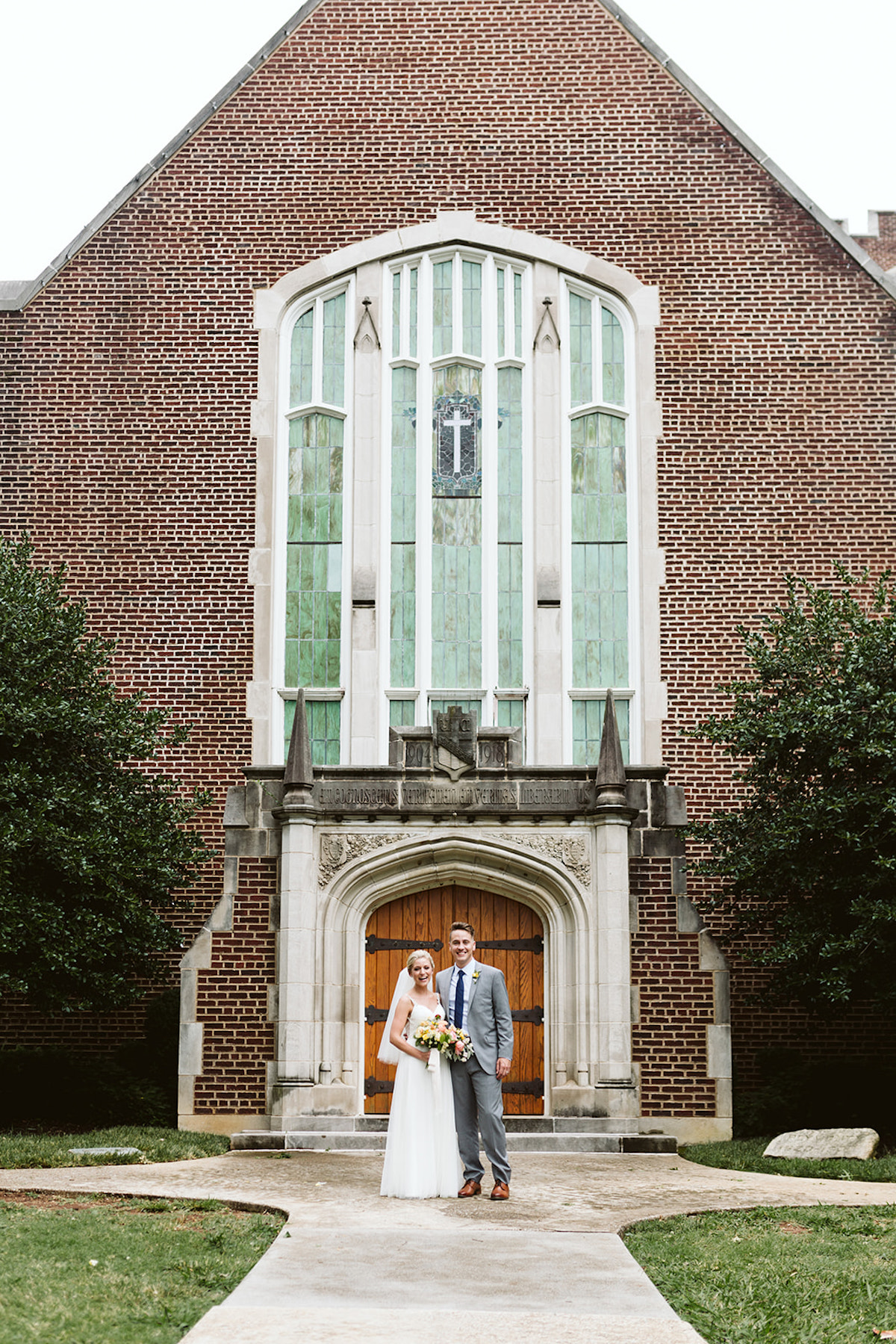 Bride and groom stand in front of Patten Chapel's wooden front door, brick exterior, and tall stained glass windows