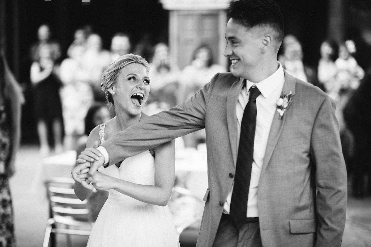 Bride holds groom's hand and looks back at him, laughing.