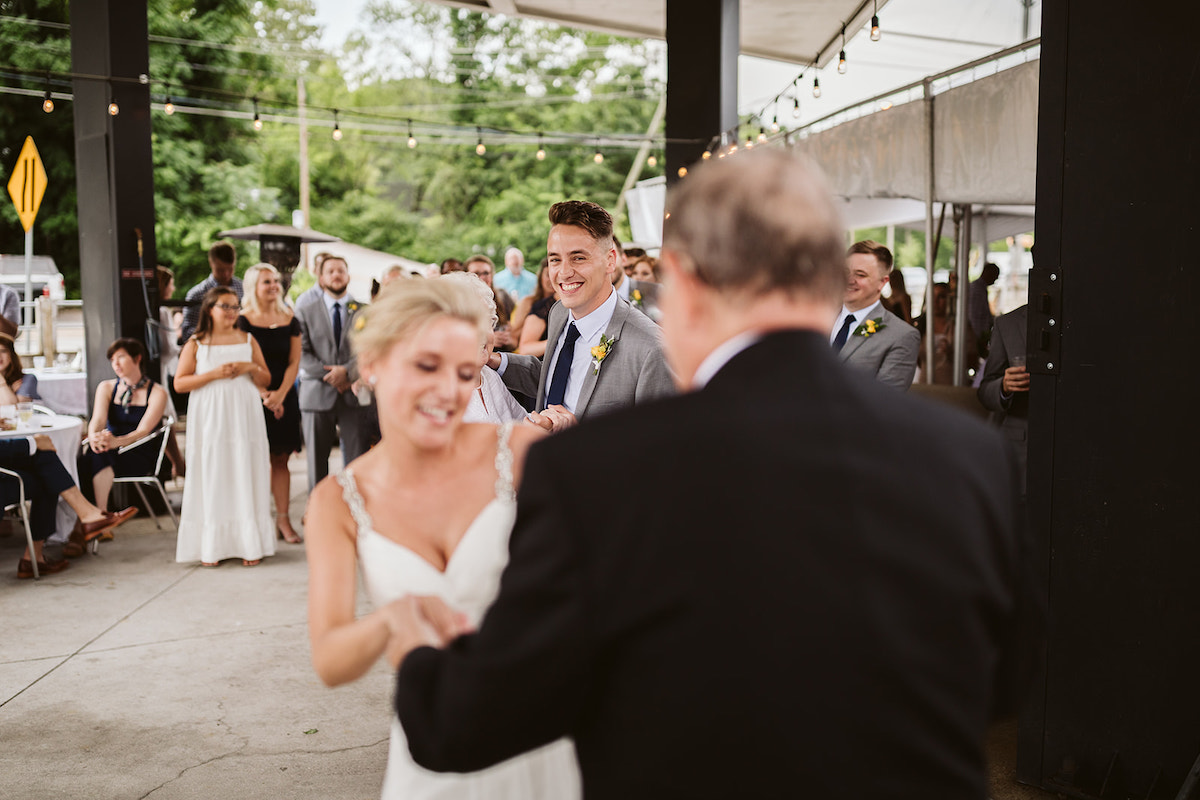 Groom smiles as he watches his bride dance with her grandfather