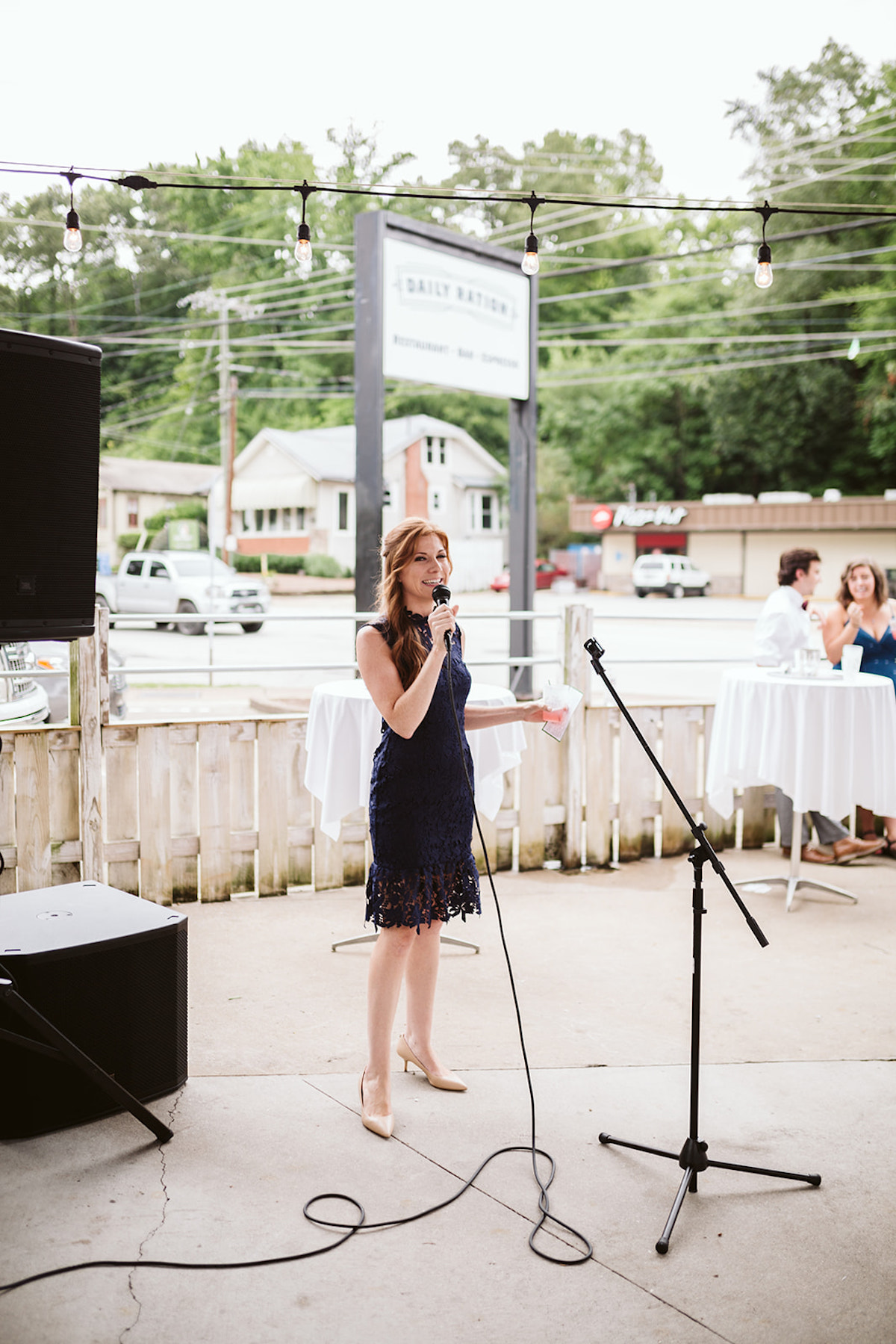 Bridesmaid in knee-length navy dress holds microphone to toast the couple