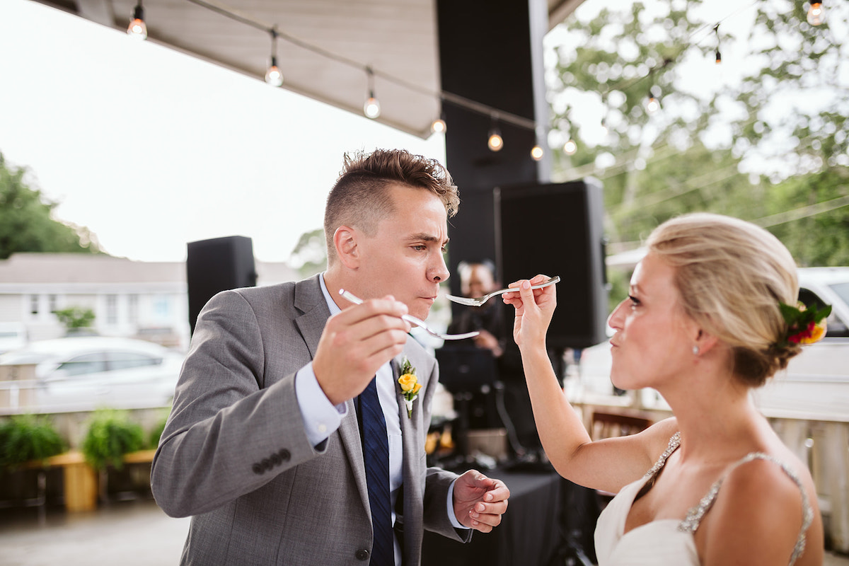 Bride and groom hold forks to each other's mouths to feed each other cake