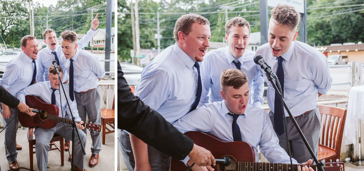 Four men wearing light blue shirts and dark blue ties stand around a microphone. One man plays guitar, and they all sing.