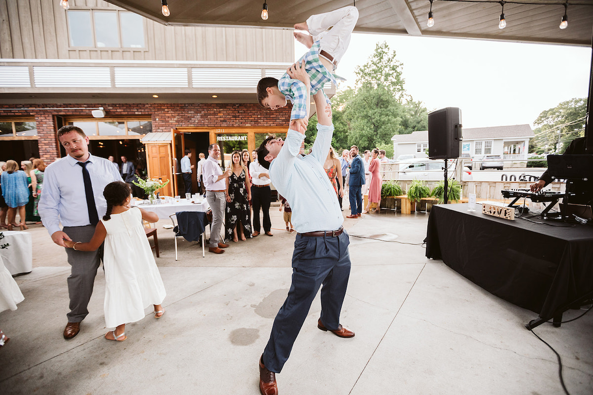Man swings young boy above his head on the dance floor under the patio cover at The Daily Ration