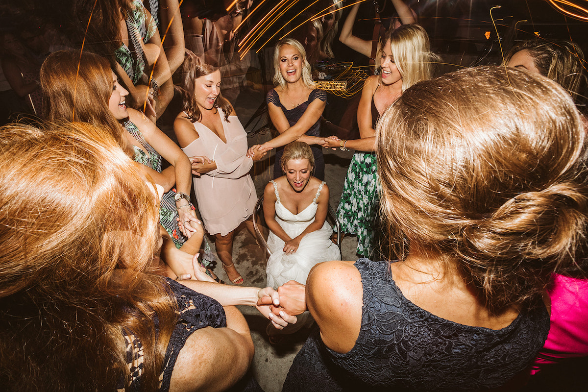 Bride crouches in the middle of a circle of women who hold hands and sing above her