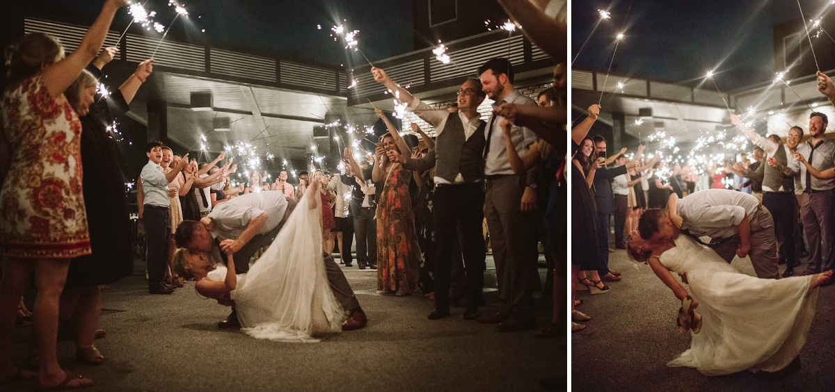 Groom dips bride low under sparkler tunnel. They look at each other while guests cheer.