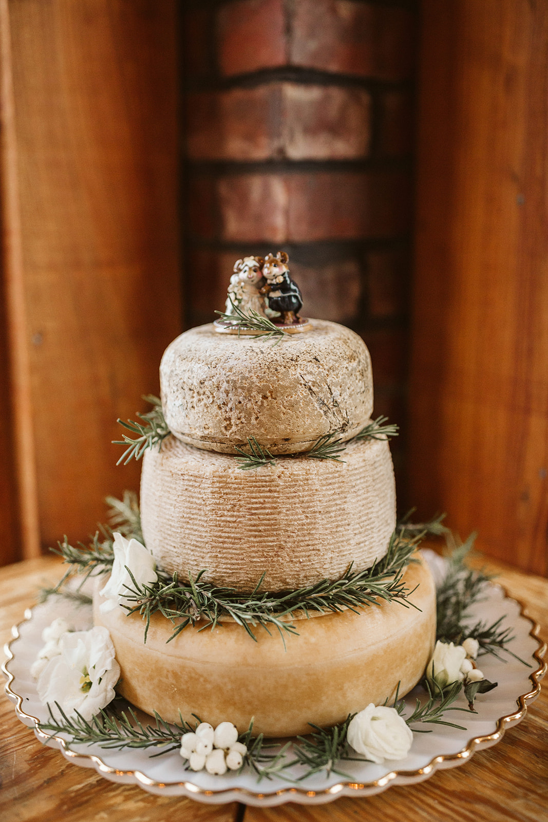 Three large cheese wheels decorated with sprigs of rosemary sit atop one another like a wedding cake.