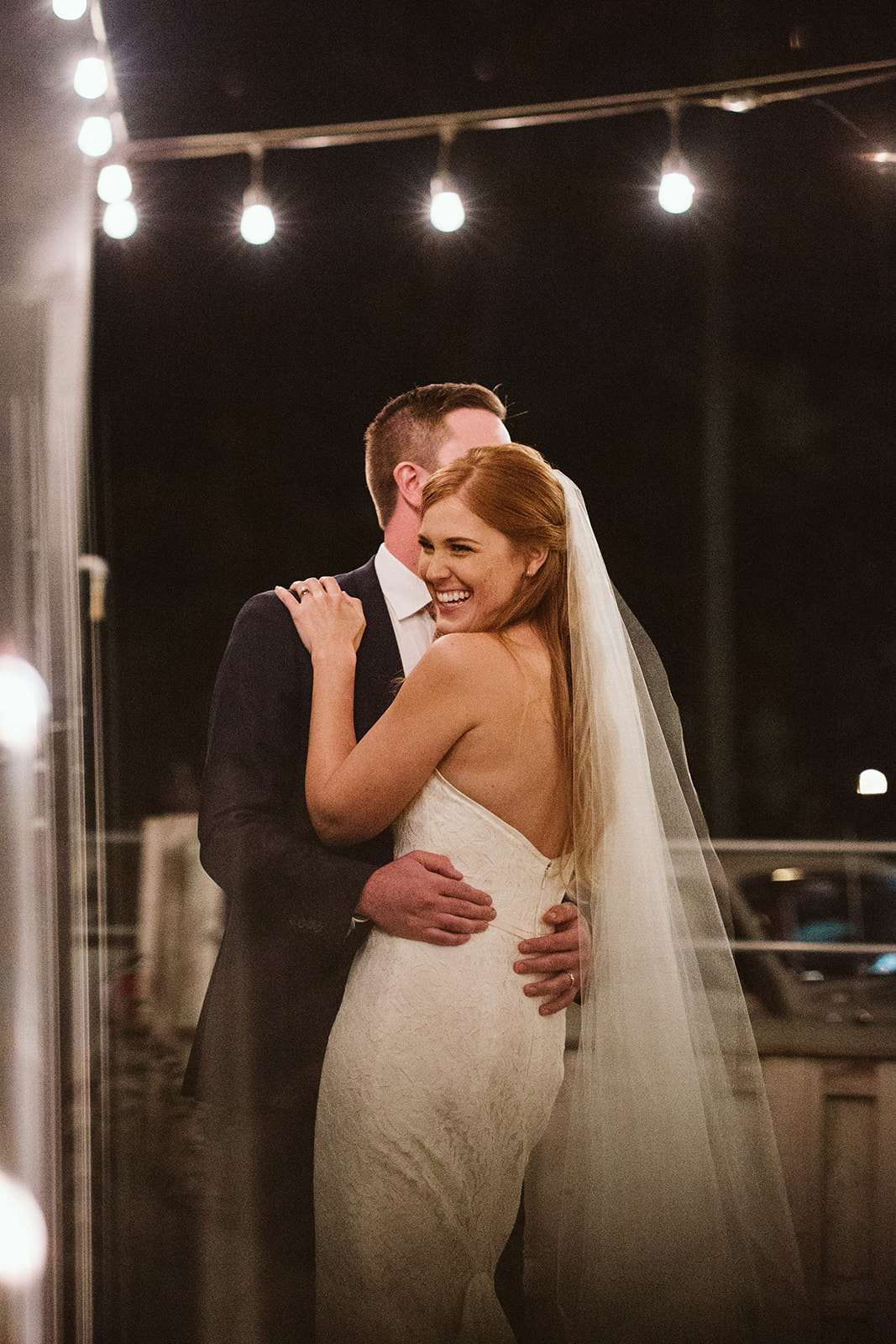 bride and groom dance under white patio lights