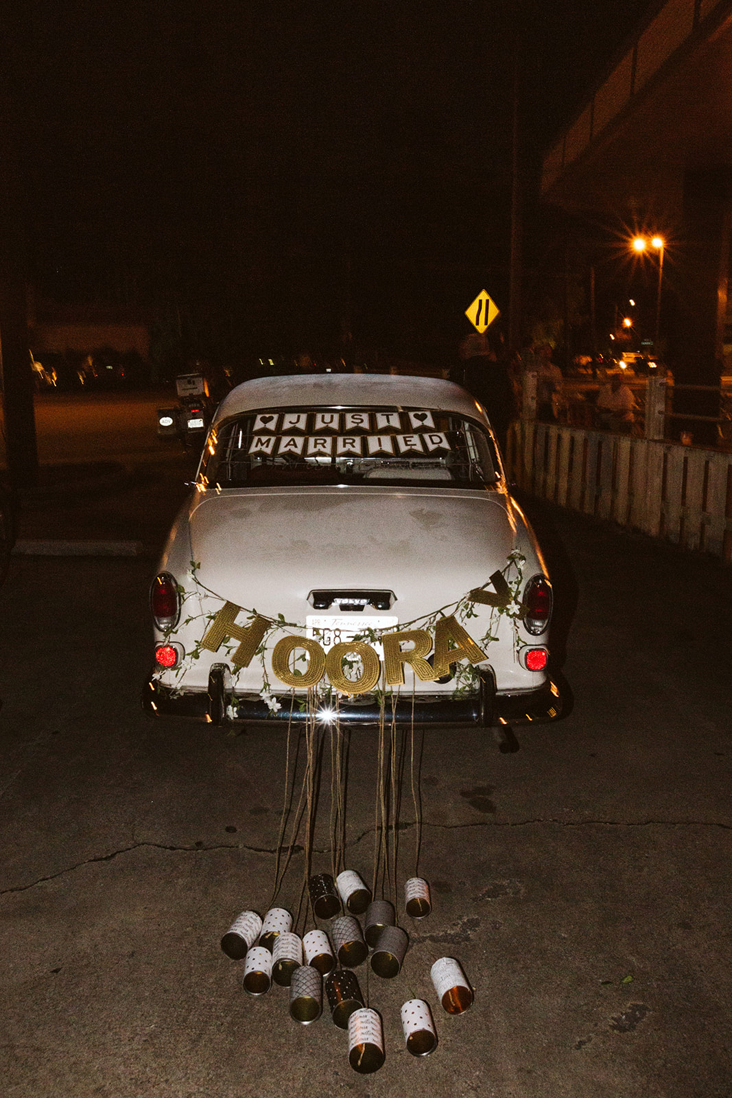 large Just married sign strung across the rear window of an antique white car. Metal cans are tied to the bumper.