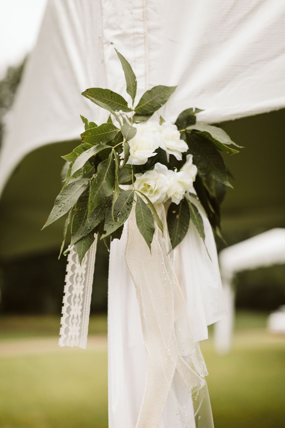 white and green wedding day flowers tied with lace at the corner of backyard wedding tent