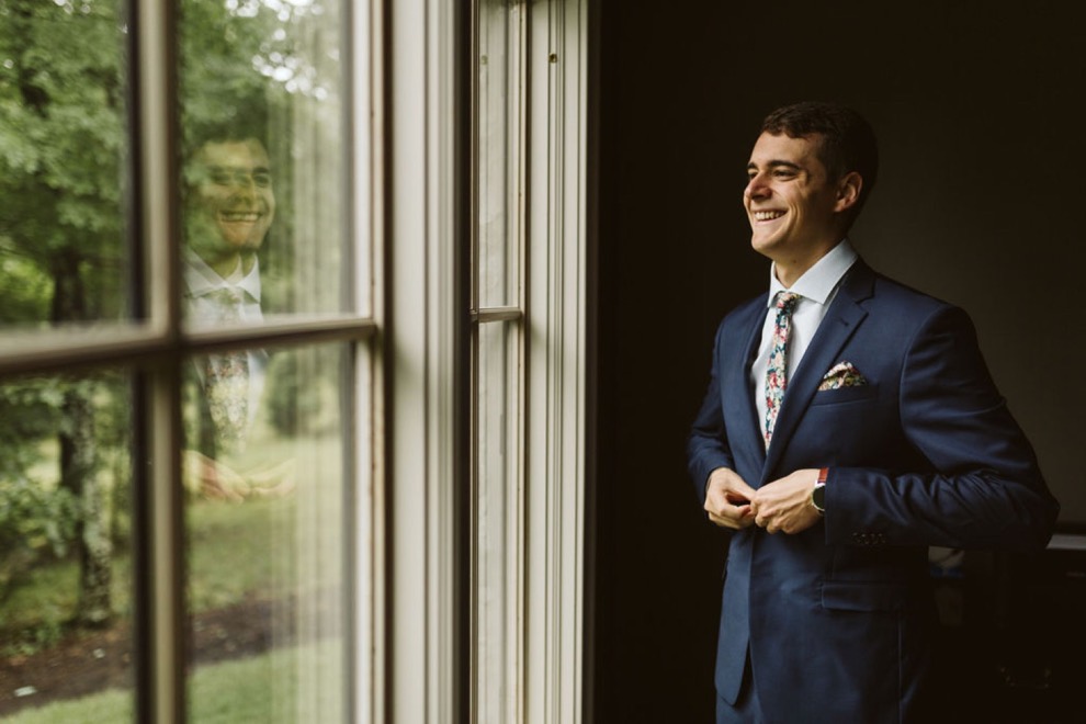 groom laughing as he buttons his dark blue suit jacket over his flower printed tie