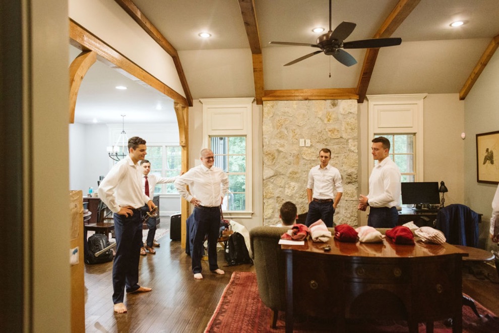 groomsmen getting ready in large room with exposed wood beams and stone fireplace