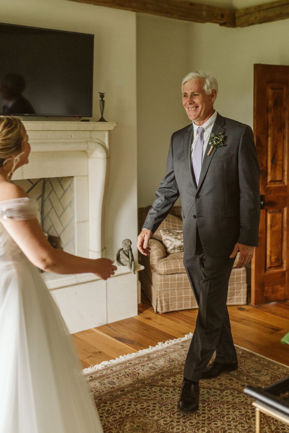 father wearing gray suit and lavender tie seeing his daughter in her wedding dress for the first time