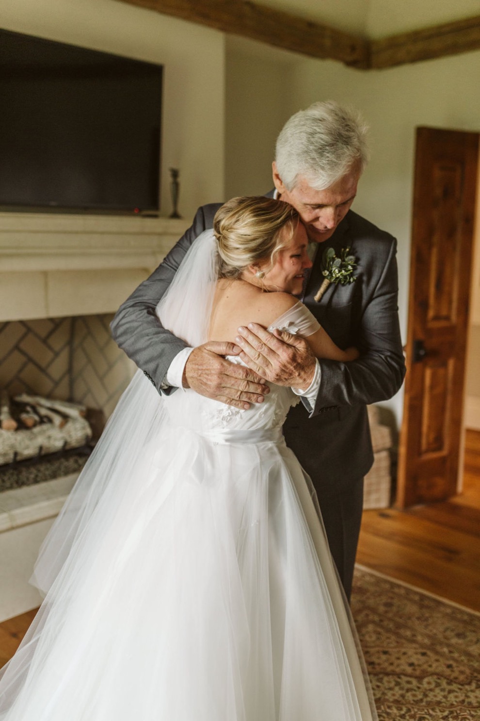 bride hugging her father in front of a fireplace