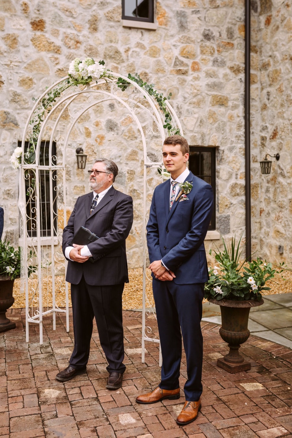 groom waiting at simple white wedding arch