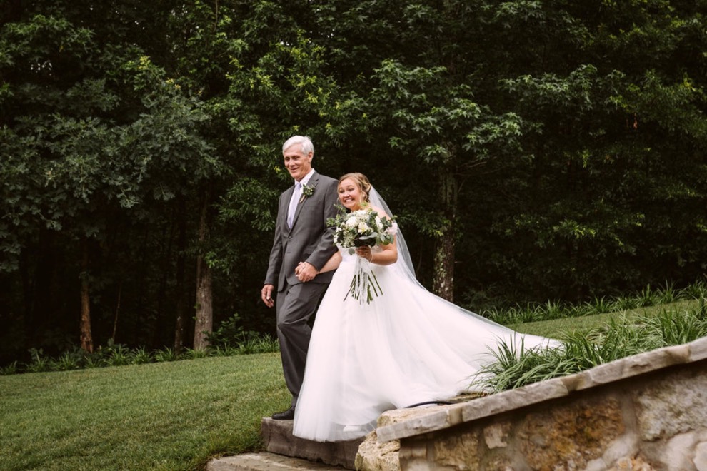 bride's father walking down large stone steps with mature oak trees behind them
