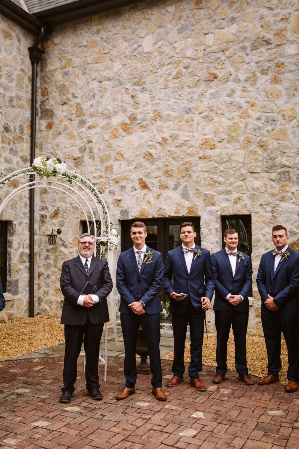 groom waiting for his bride at wedding arch in the courtyard of a stone house