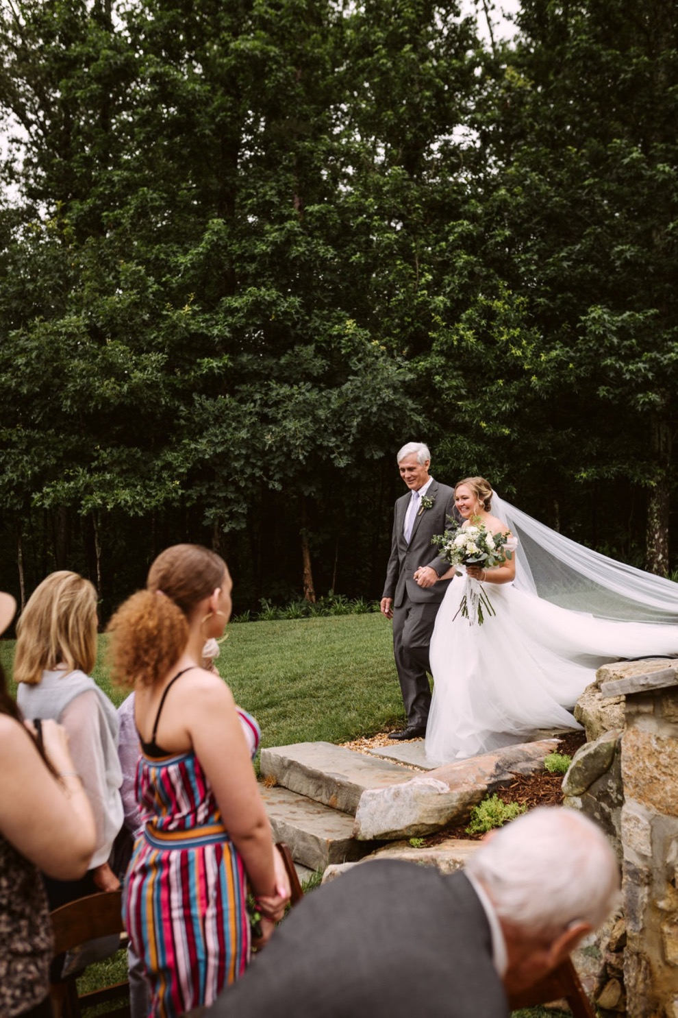 bride's father escorts her down large stone steps as her long veil trails behind her