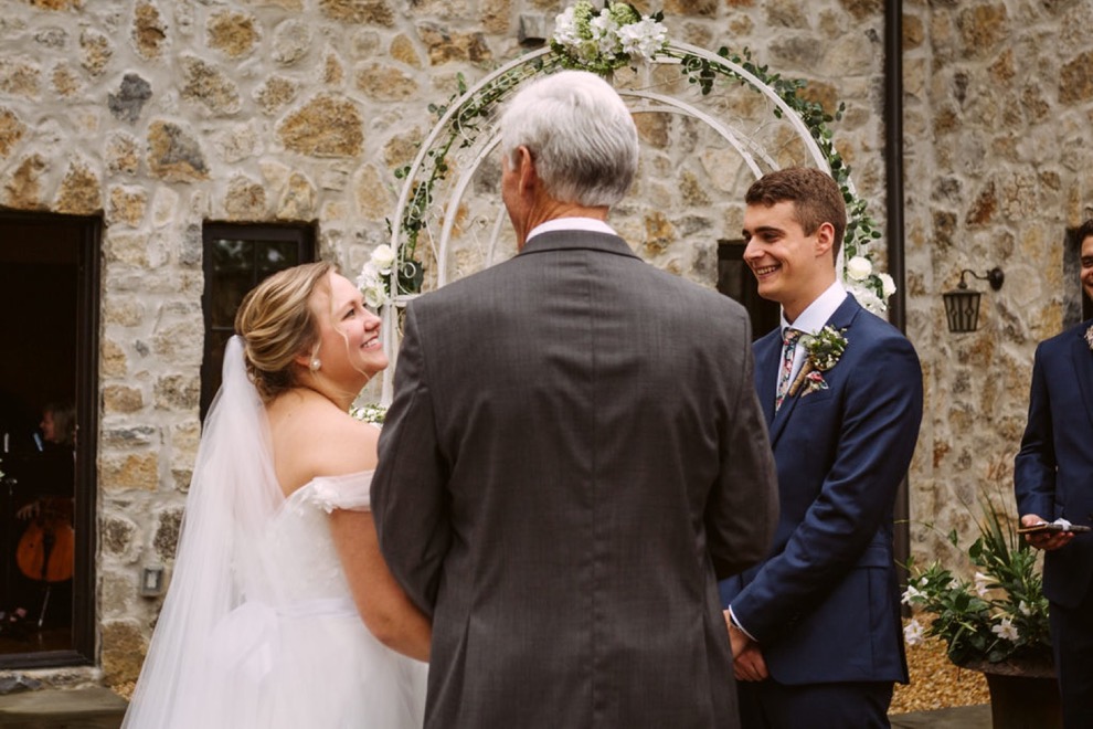 bride smiles at her father as he gives her hand to her groom