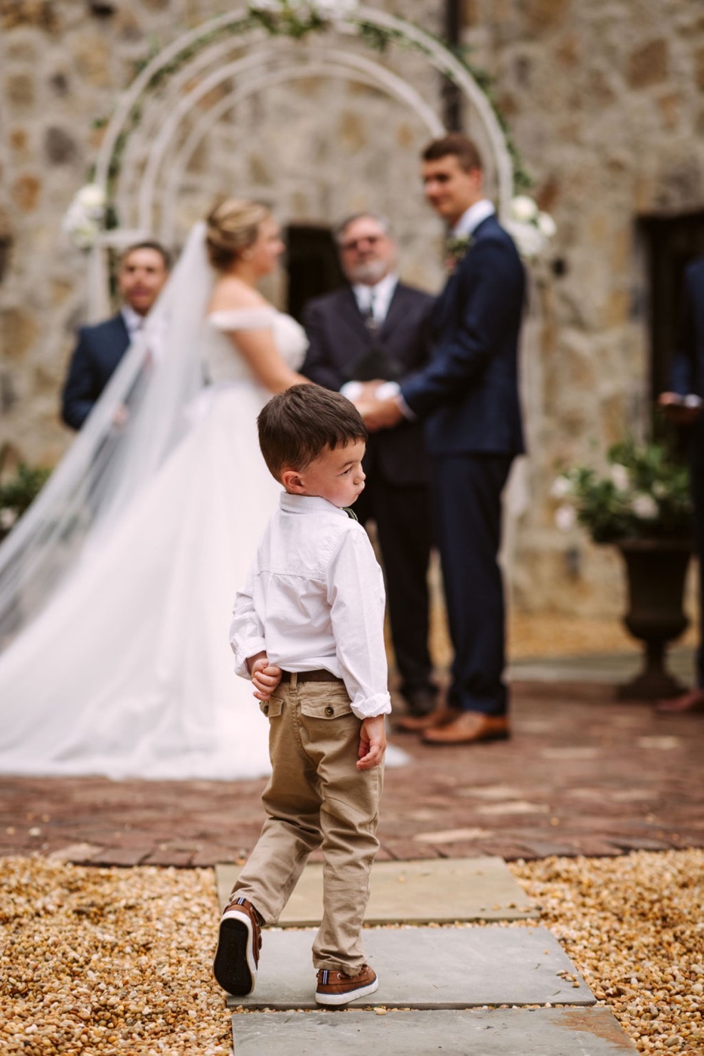 ring bearer standing on a stone paver path during wedding ceremony