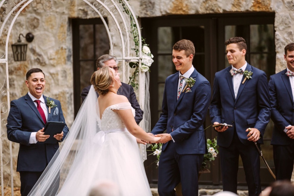 bride and groom laughing as officiant speaks to them and wedding guests