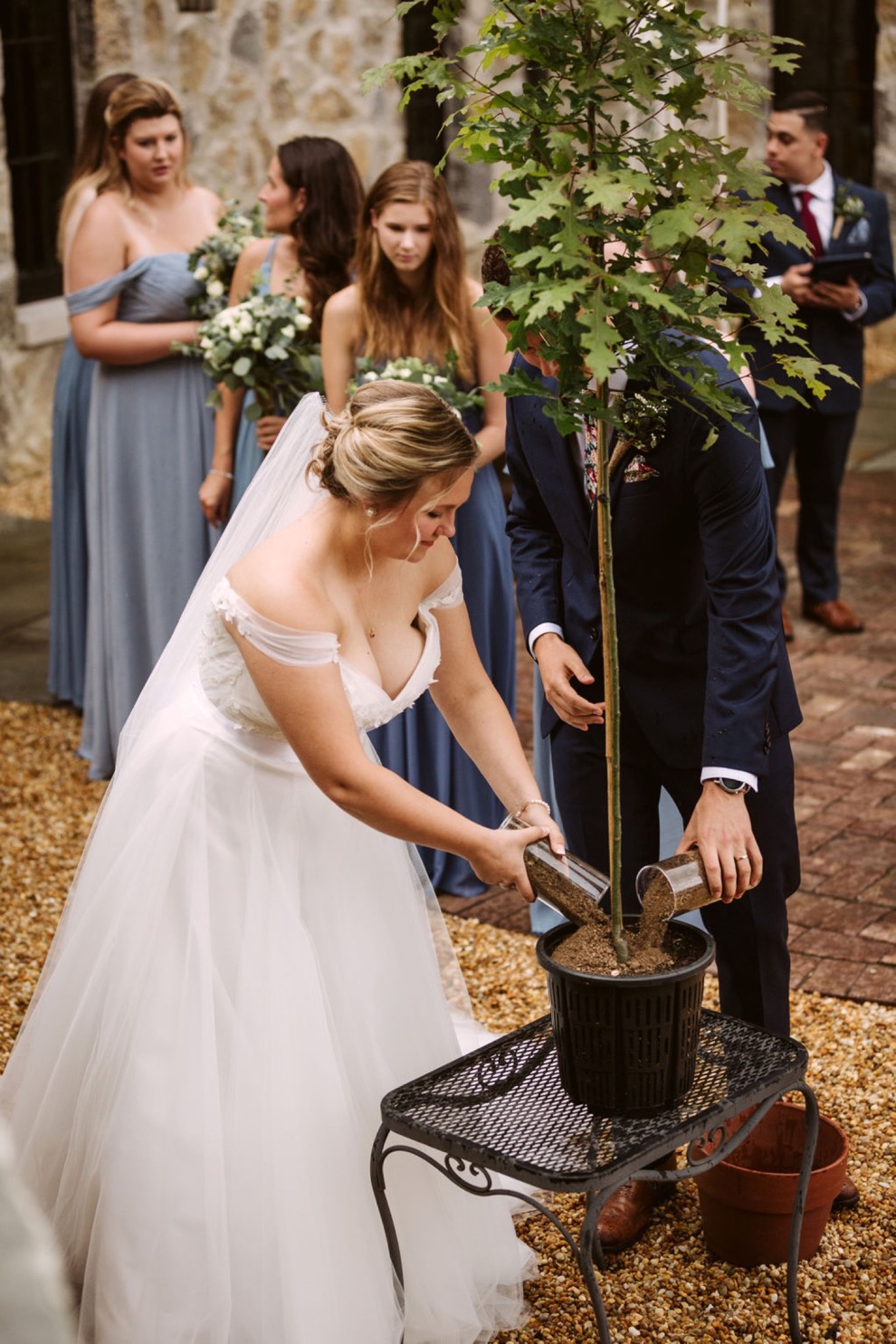 bride and groom adding dirt to an oak sapling during their backyard wedding