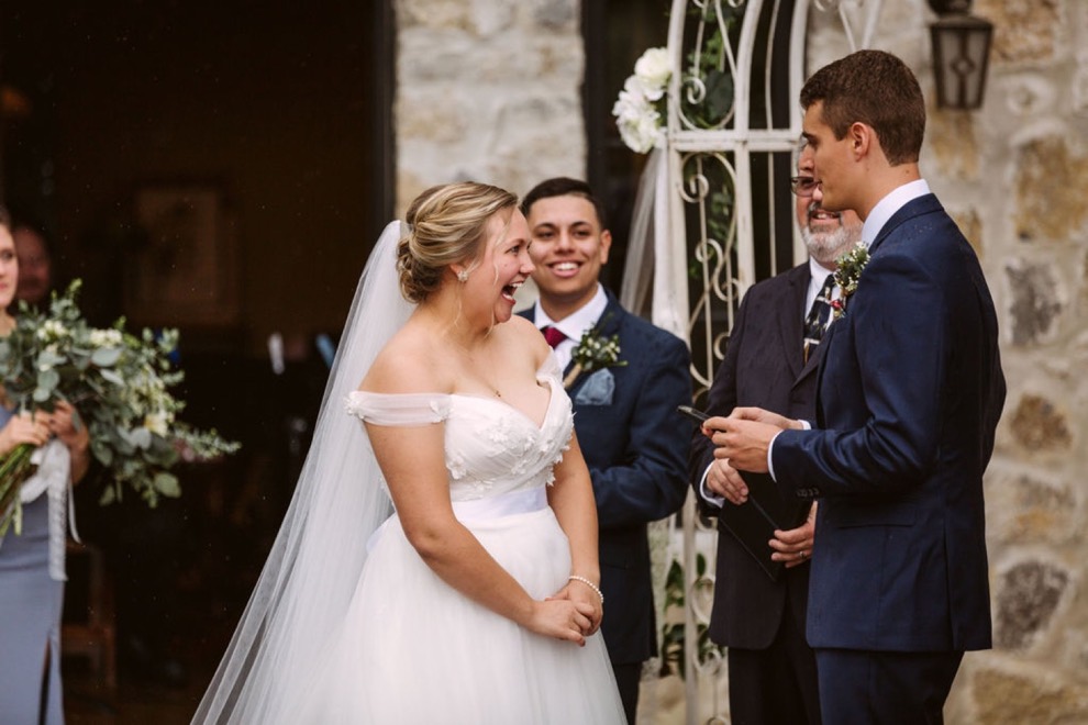 bride laughing as groom reads his vows to her from his phone