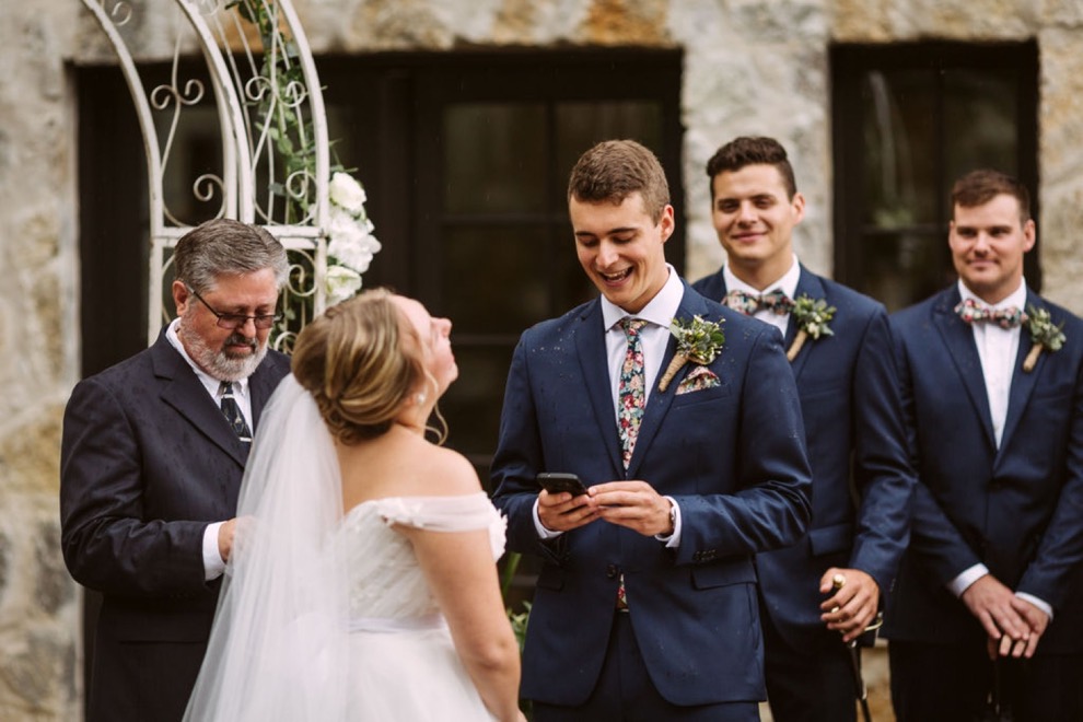 bride and groom laughing as he reads his wedding vows from his phone