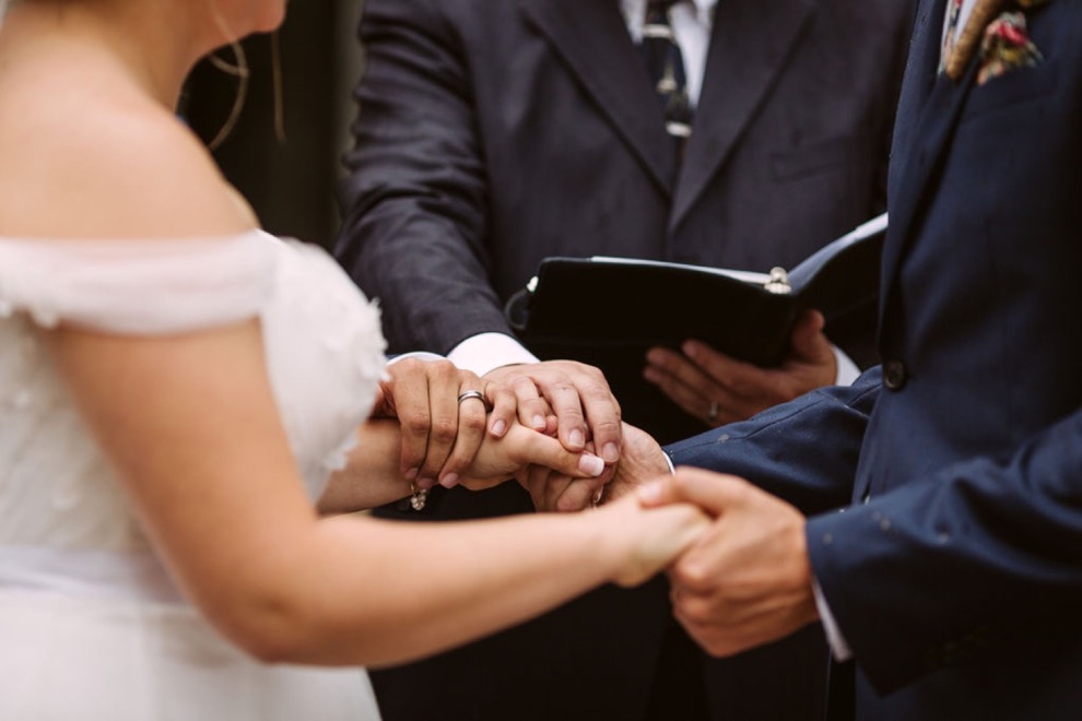 bride and groom holding hands as minister places his hand on both of theirs