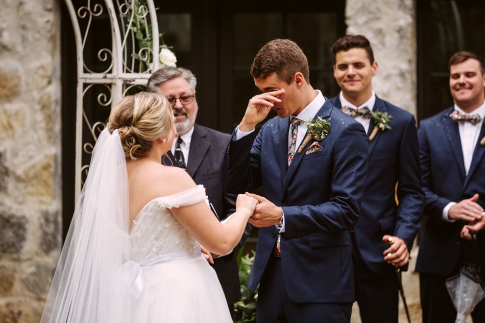 groom wiping tears away during ceremony as bride holds his hand