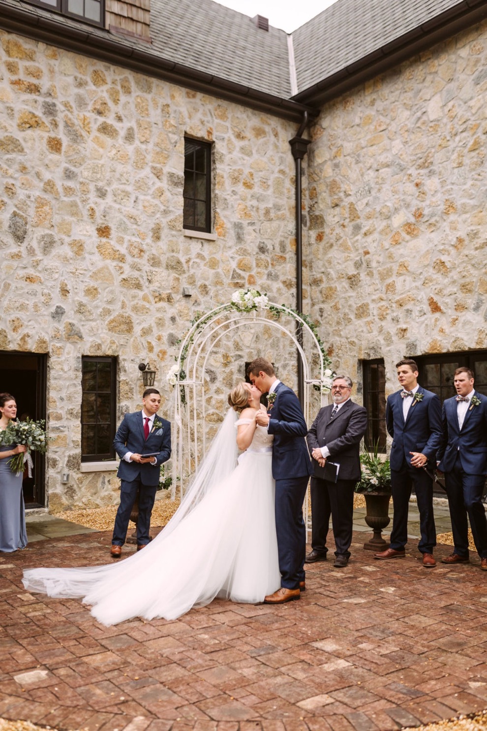 bride and groom kissing in the courtyard of a large stone house during backyard wedding ceremony