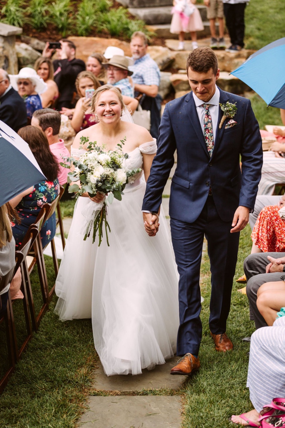 bride and groom smiling as they walk a stone path between wedding guests