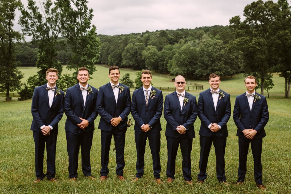 groomsmen posing in a large grass field for portraits