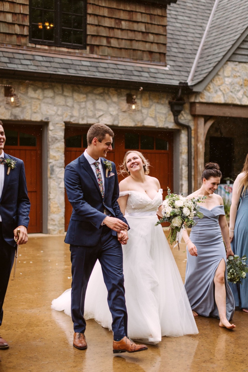 bride and groom walking with bridal party away from a stone estate house