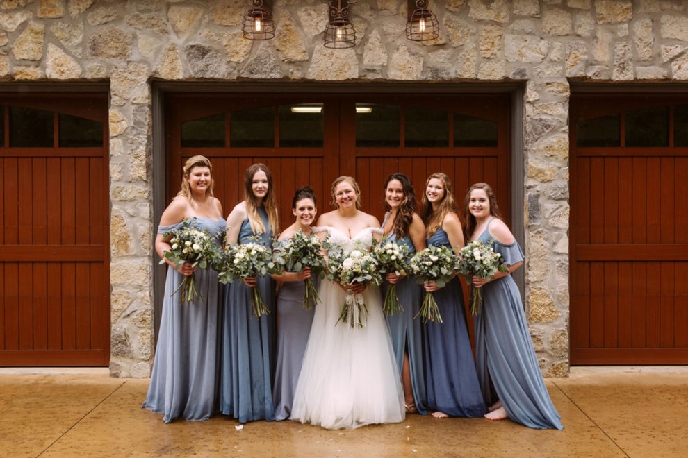 bride with bridesmaids laughing together in front of wide wooden garage door