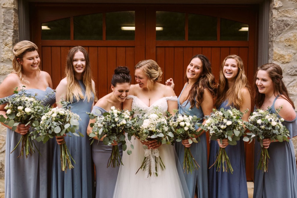 bride with bridesmaids laughing together in front of wide wooden garage door