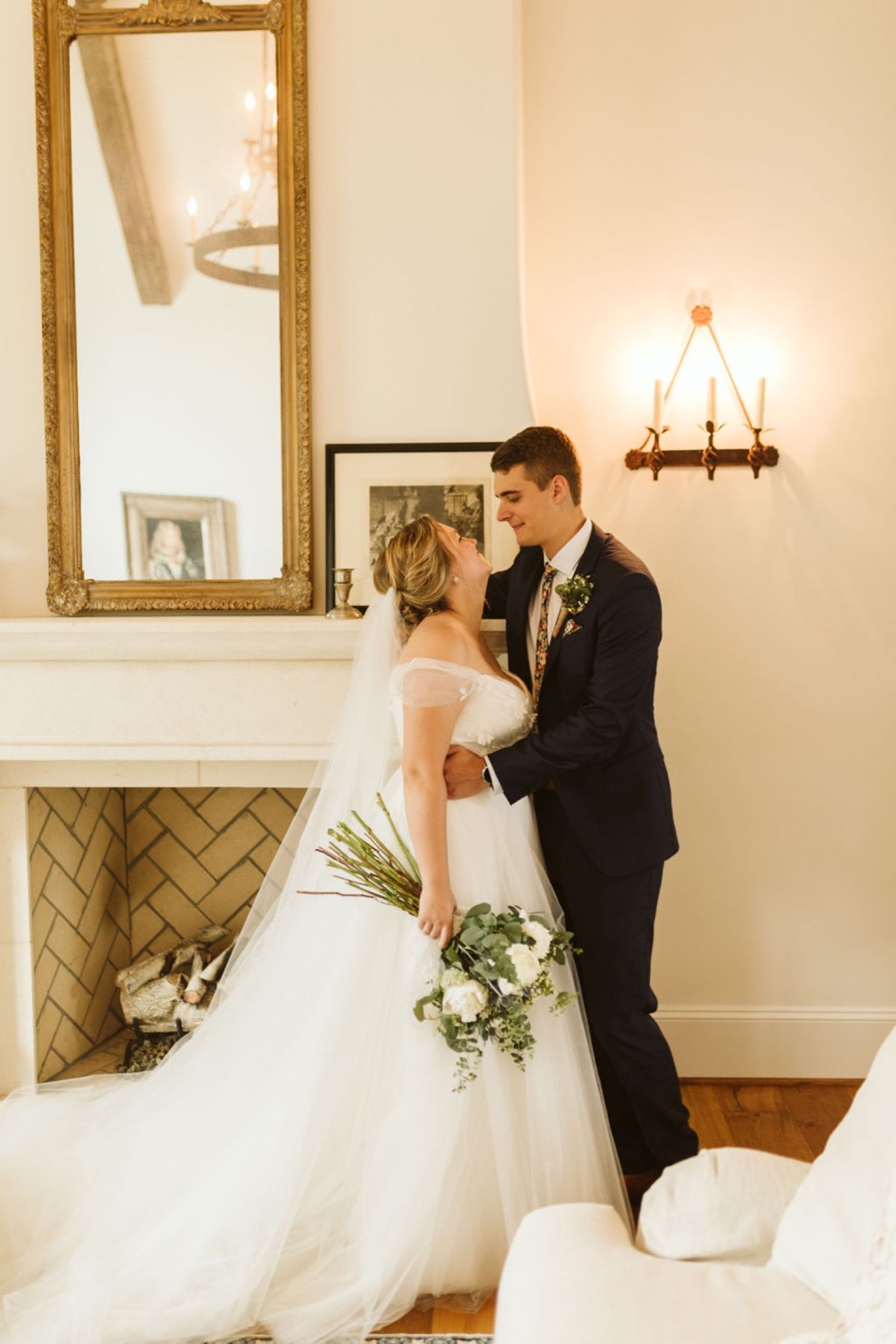 bride and groom smiling at each other in front of a tall fireplace in a Georgia estate