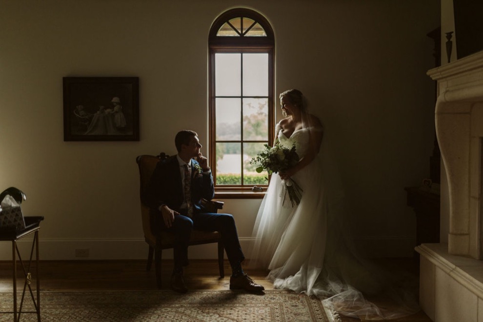 bride and groom sitting in front of window in dimly lit room