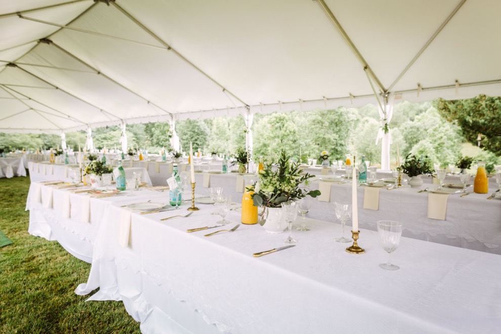 white lace-covered long tables set with tapered candles and glass carafes of orange juice under a white tent