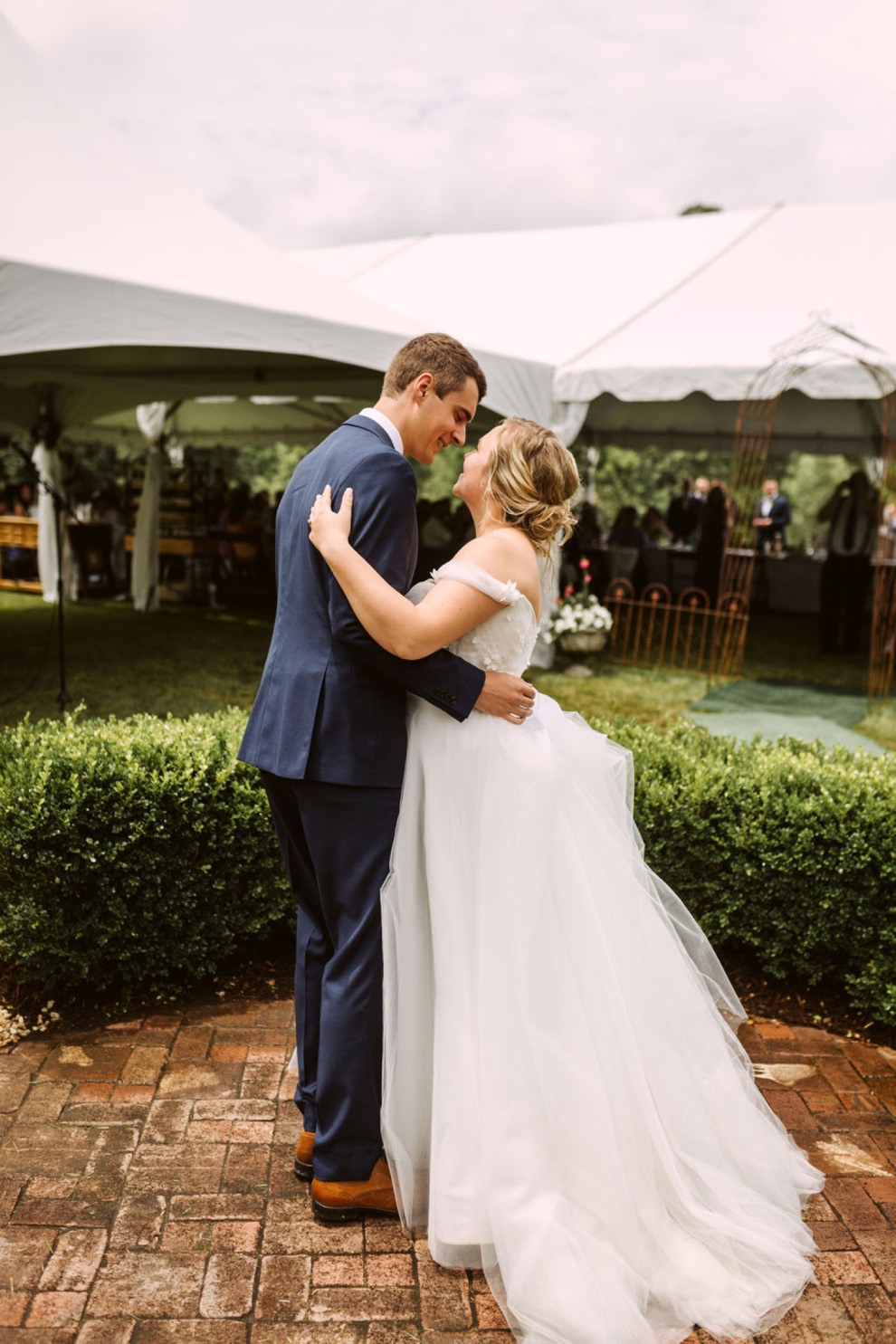 bride and groom dancing on a brick patio surrounded by low green hedge