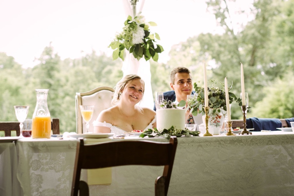 bride and groom sit at a white lace-covered table and smile