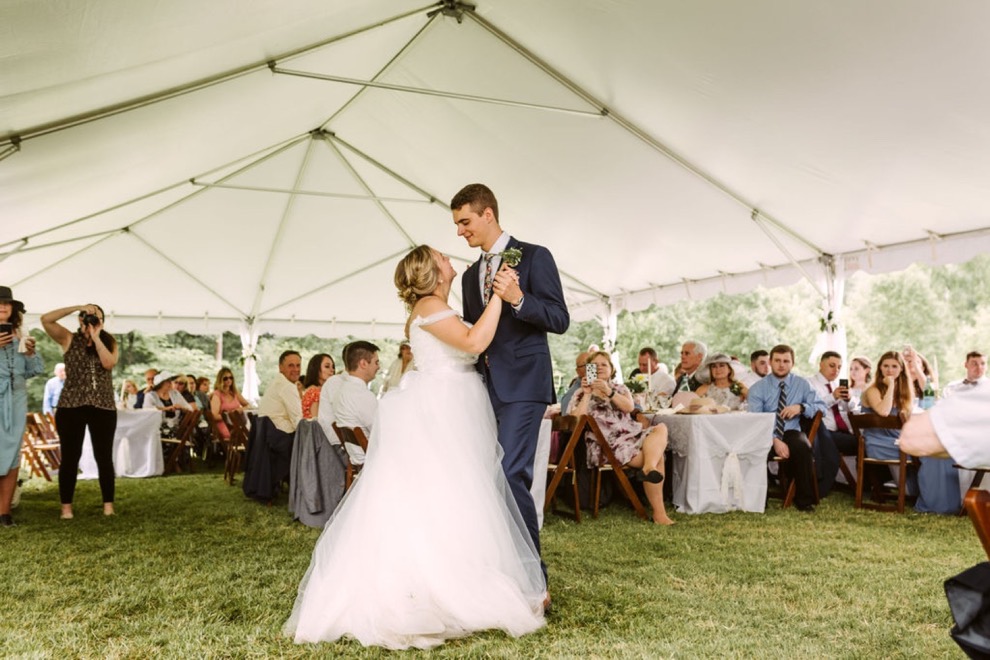 bride and groom first dance on grass under large, white tent during their backyard wedding reception