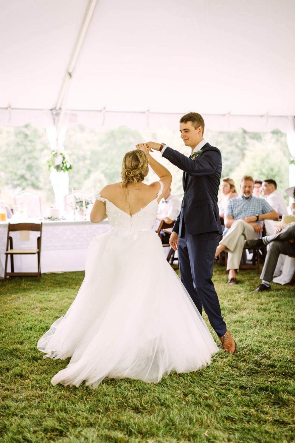 bride and groom first dance on grass under large, white tent during their backyard wedding reception