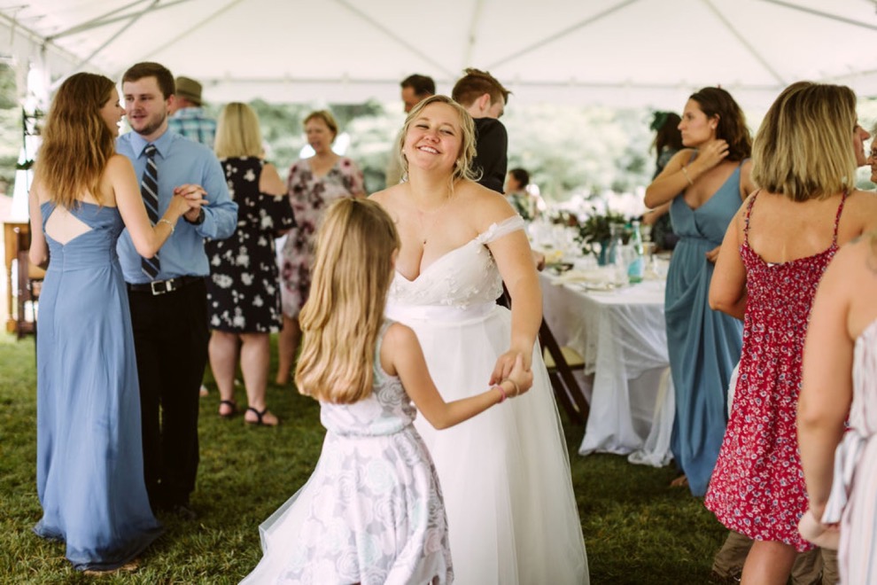 Bride dancing with young girl and other guests on grass under large, white tent