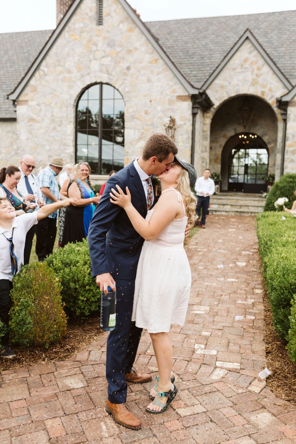 bride and groom kissing on brick pathway in front of stone house